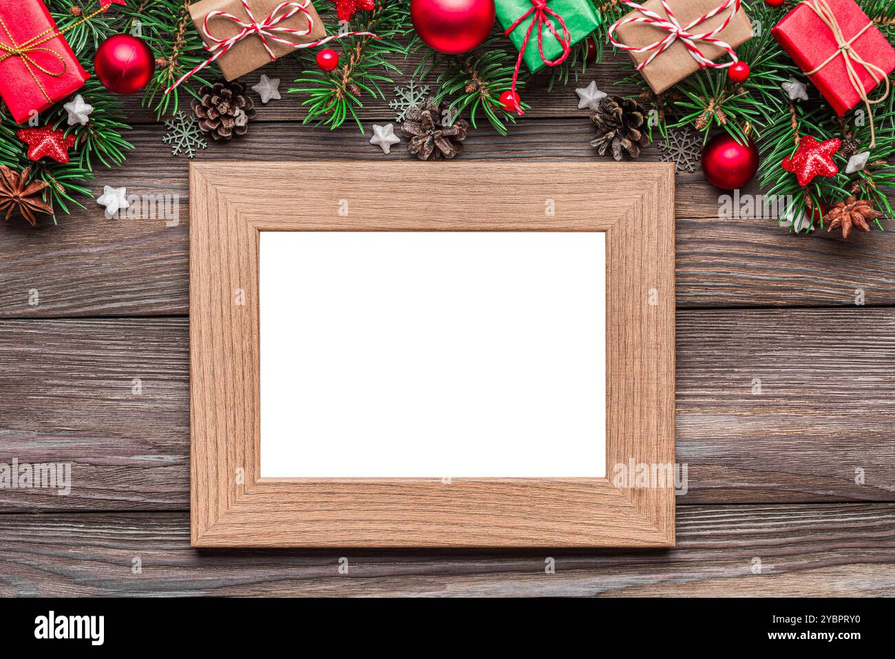 Cadre photo vierge avec décorations de Noël, branches de sapin, boîtes cadeaux et pommes de pin sur une table en bois rustique. Pose à plat. Maquette. Bonne année Banque D'Images