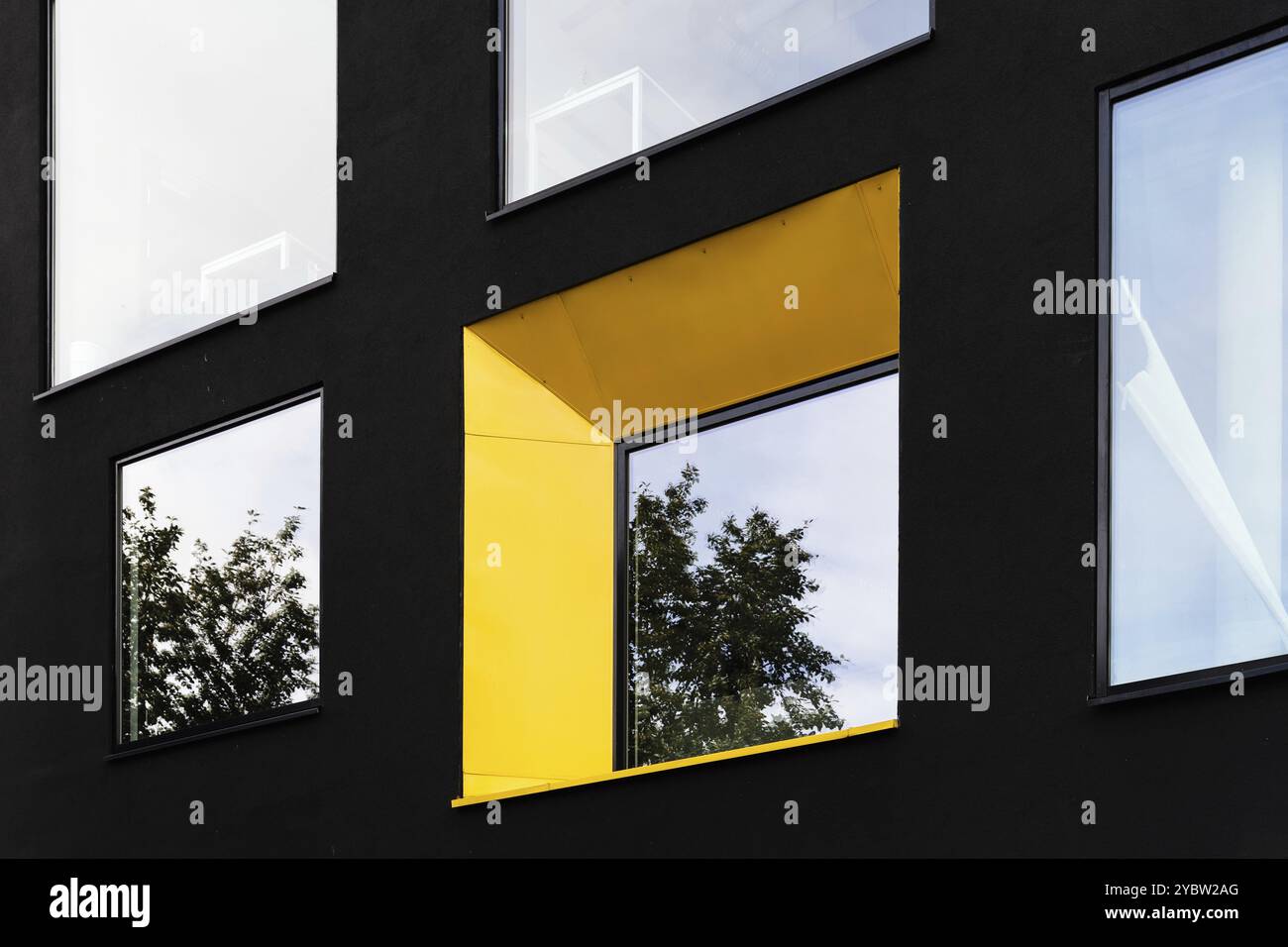 Fenêtre jaune sur façade noire avec reflet de l'arbre vert. Arrière-plan de l'architecture abstraite Banque D'Images