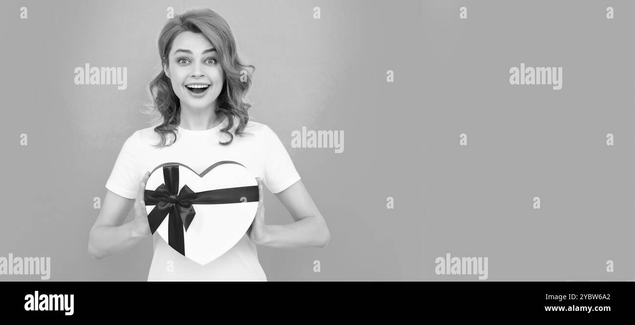 boîte cadeau coeur de main de fille stupéfait sur fond bleu. Femme isolé visage portrait, bannière avec maquette d'espace de copie. Banque D'Images