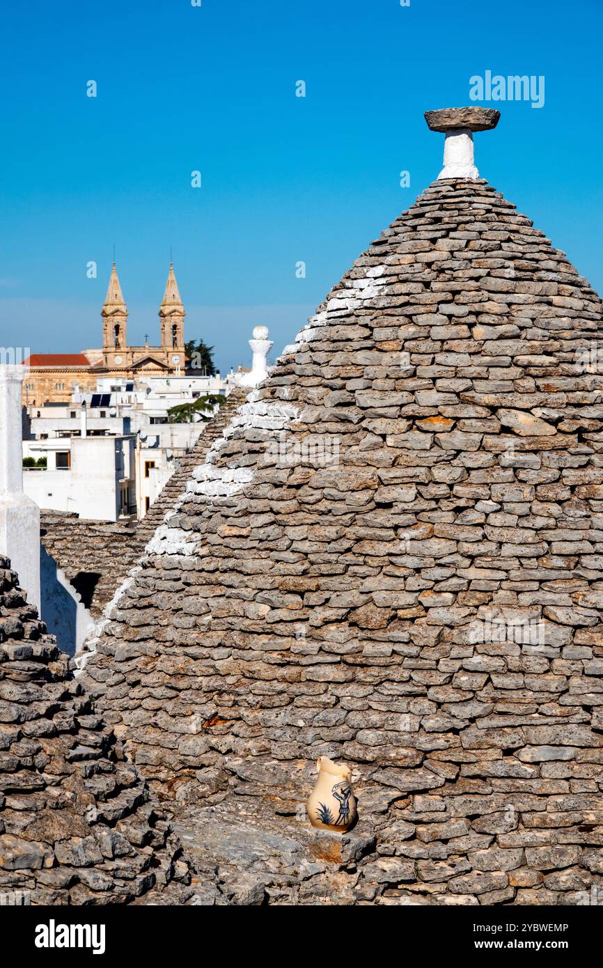 Gros plan du toit en pierre d'un trullo avec la Basilique dei Santi Medici en arrière-plan, Alberobello, Italie. Banque D'Images