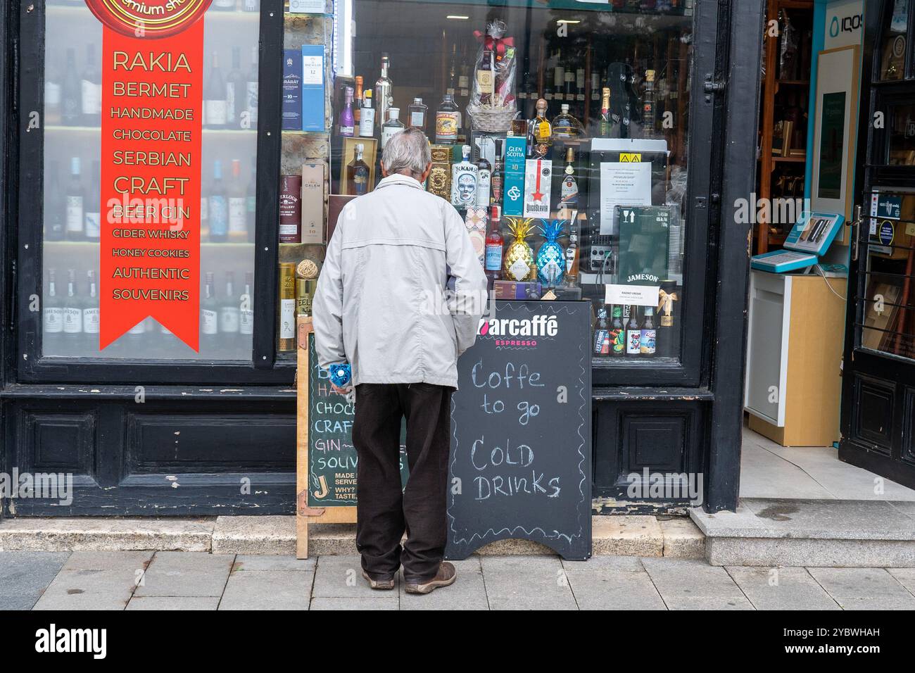 Réflexions du temps : un homme âgé observant la vitrine d'un magasin d'alcool local Banque D'Images