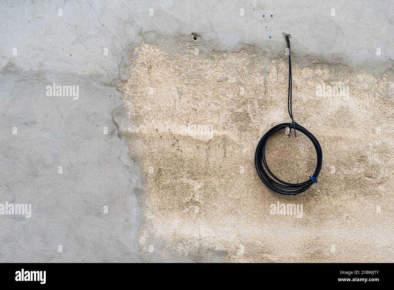 Contraste circulaire : bobine de câble noire contre mur vieilli Banque D'Images