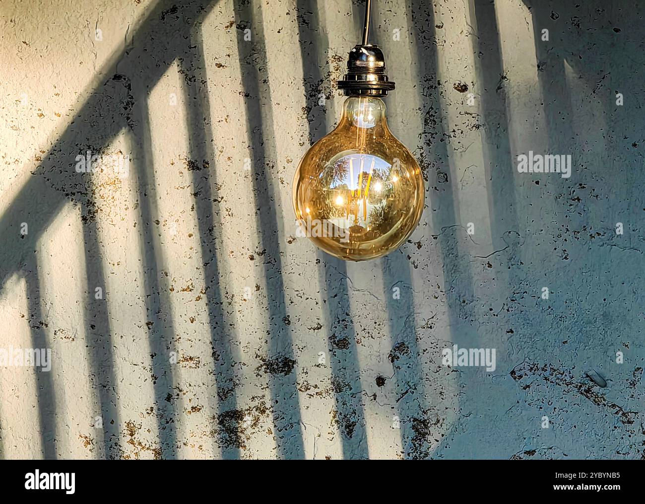Soyez la lumière dans le noir : ampoule contre les ombres sur un mur avec fond de clôture. Banque D'Images