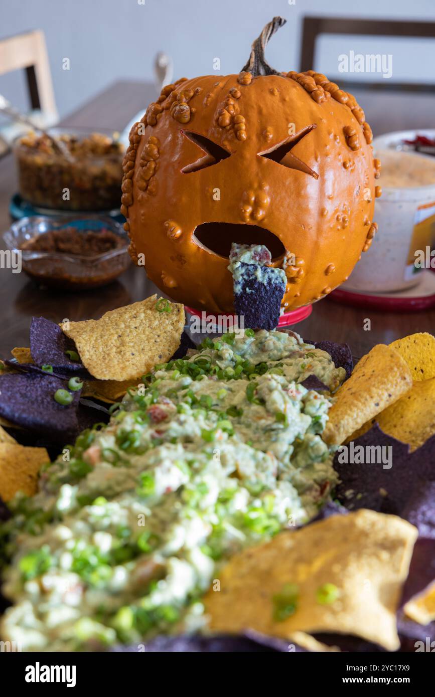 Une citrouille à l'air malade jetant des trucs verts sur une assiette de chips comme décoration de pièce centrale de table. Banque D'Images