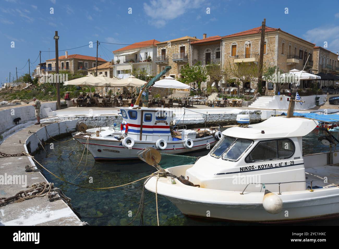 Port avec bateaux de pêche et bâtiments méditerranéens en arrière-plan. Journée ensoleillée avec restaurants et ciel bleu, Agios Nikolaos, Mani, Messenia, Pel Banque D'Images