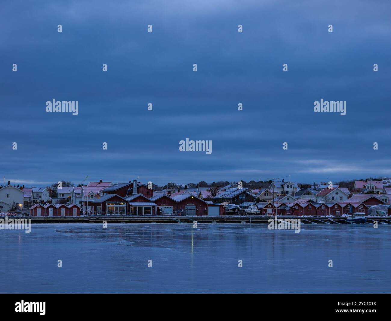 Au crépuscule, le port de Hönö révèle de charmants bâtiments reflétant la tranquillité sur des eaux calmes. Les teintes bleues douces créent une atmosphère sereine et être Banque D'Images