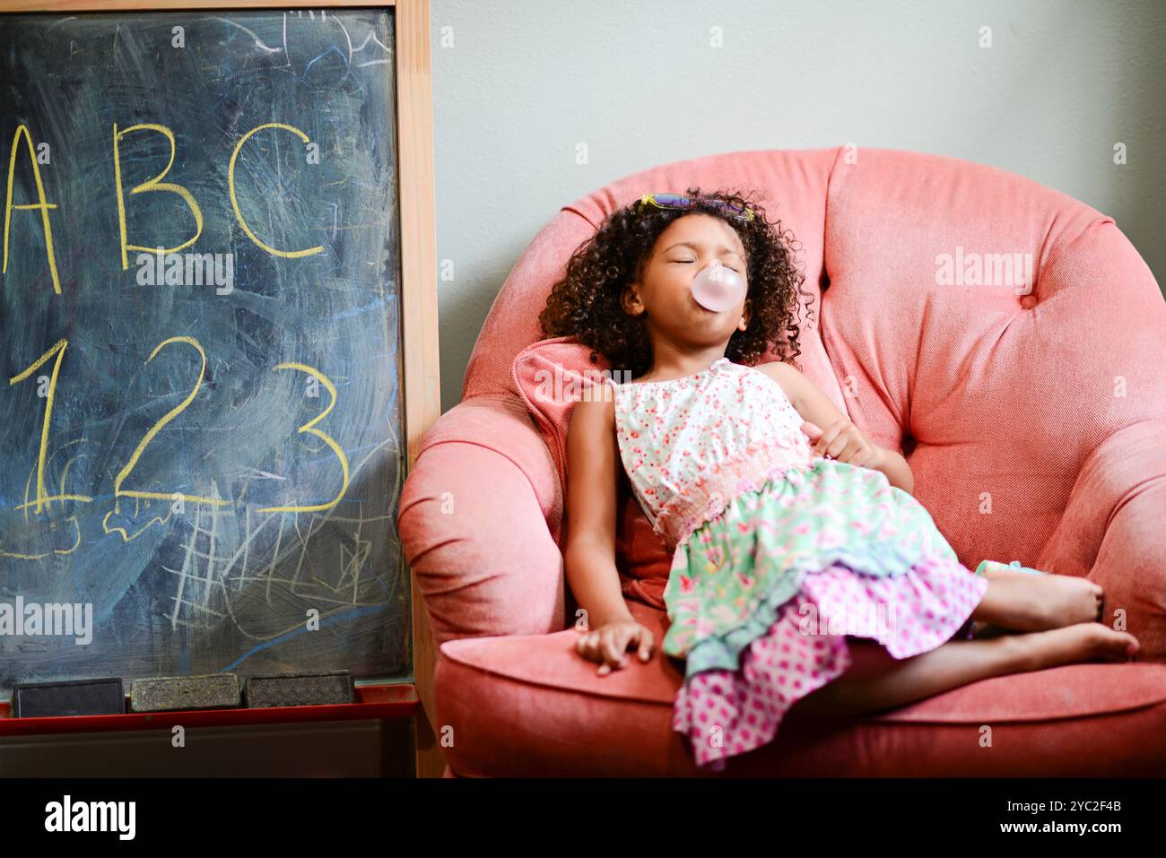 Jeune fille se relaxant sur une chaise rose, soufflant une bulle avec de la bulle Banque D'Images