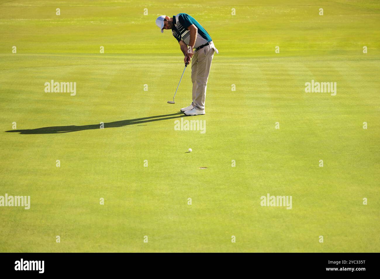 Un golfeur se concentre sur son jeu court sur un terrain de golf luxuriant, visant un putt réussi par une journée ensoleillée. Banque D'Images