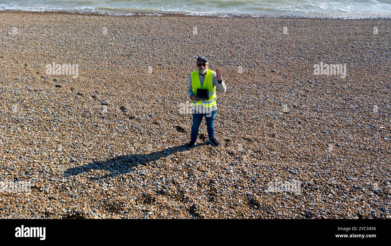 Pilote de drone senior prenant un selfie et agitant, alors qu'il ramène le drone vers le bas pour un atterrissage sur Walmer Beach, Kent. Banque D'Images