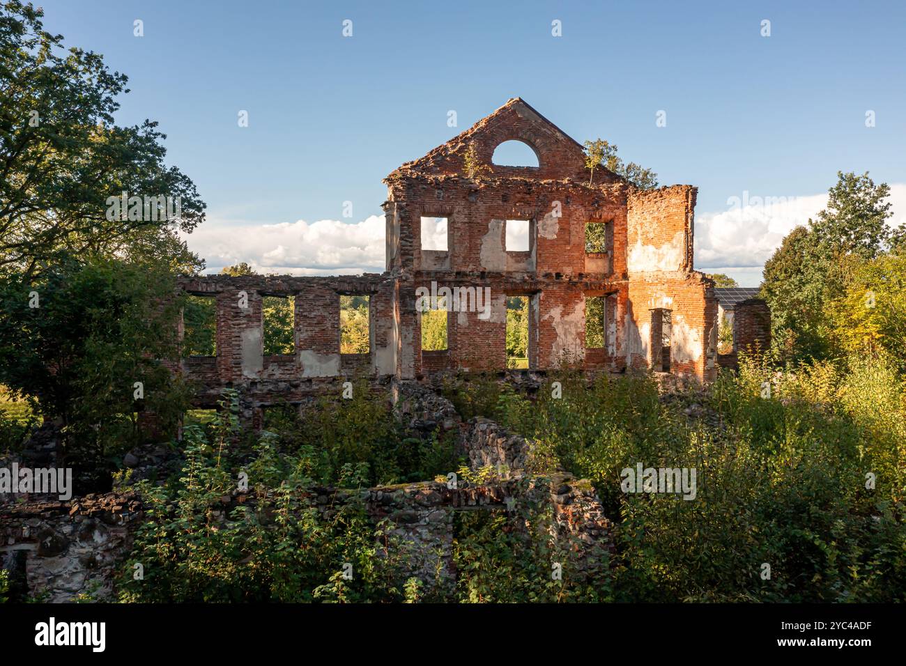 Une structure de briques se trouve en ruines, dépassée par la verdure sous un ciel clair. Banque D'Images