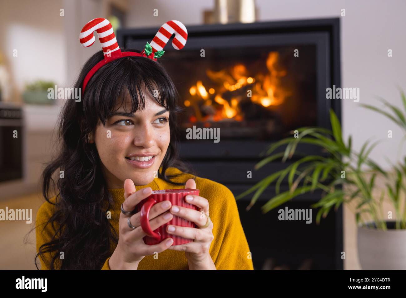 Temps de Noël, femme portant bandeau festif profitant d'une boisson chaude par cheminée confortable à la maison Banque D'Images