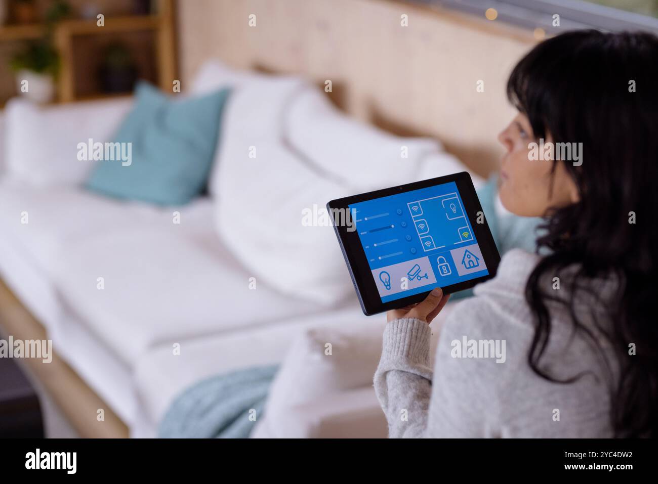 Femme utilisant une tablette pour contrôler les appareils domestiques intelligents dans un salon confortable Banque D'Images