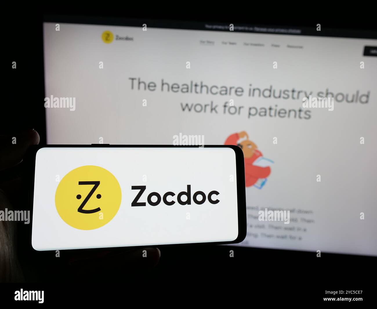 Personne tenant un smartphone avec le logo de la société américaine de télémédecine Zocdoc Inc sur l'écran en face du site Web. Concentrez-vous sur l'affichage du téléphone. Banque D'Images