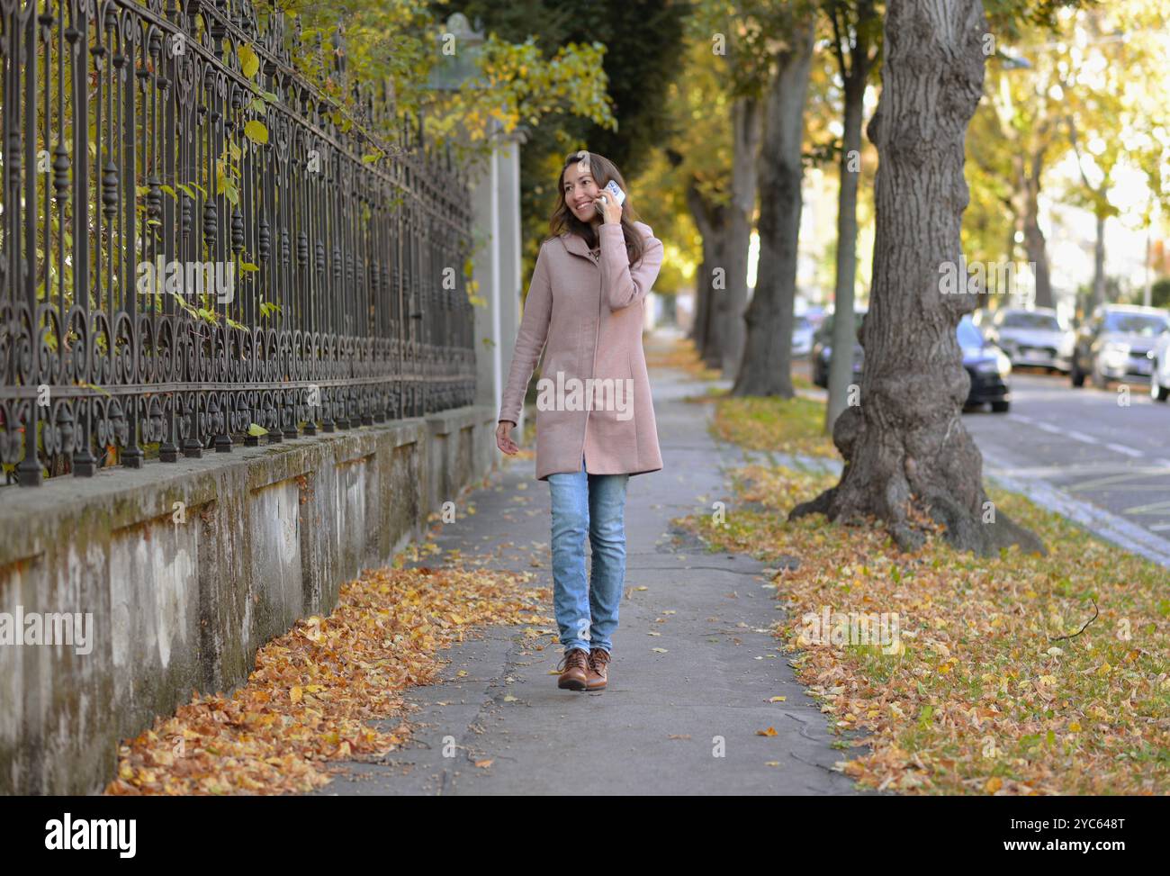 Une femme parlant au téléphone dans la rue par un jour ensoleillé d'automne. Une femme sourit en utilisant un smartphone mobile. Banque D'Images