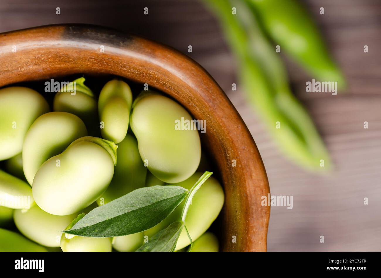 Fèves de Fava fraîches et quelques feuilles de fèves de Fava dans un bol en argile sur un fond en bois. Banque D'Images