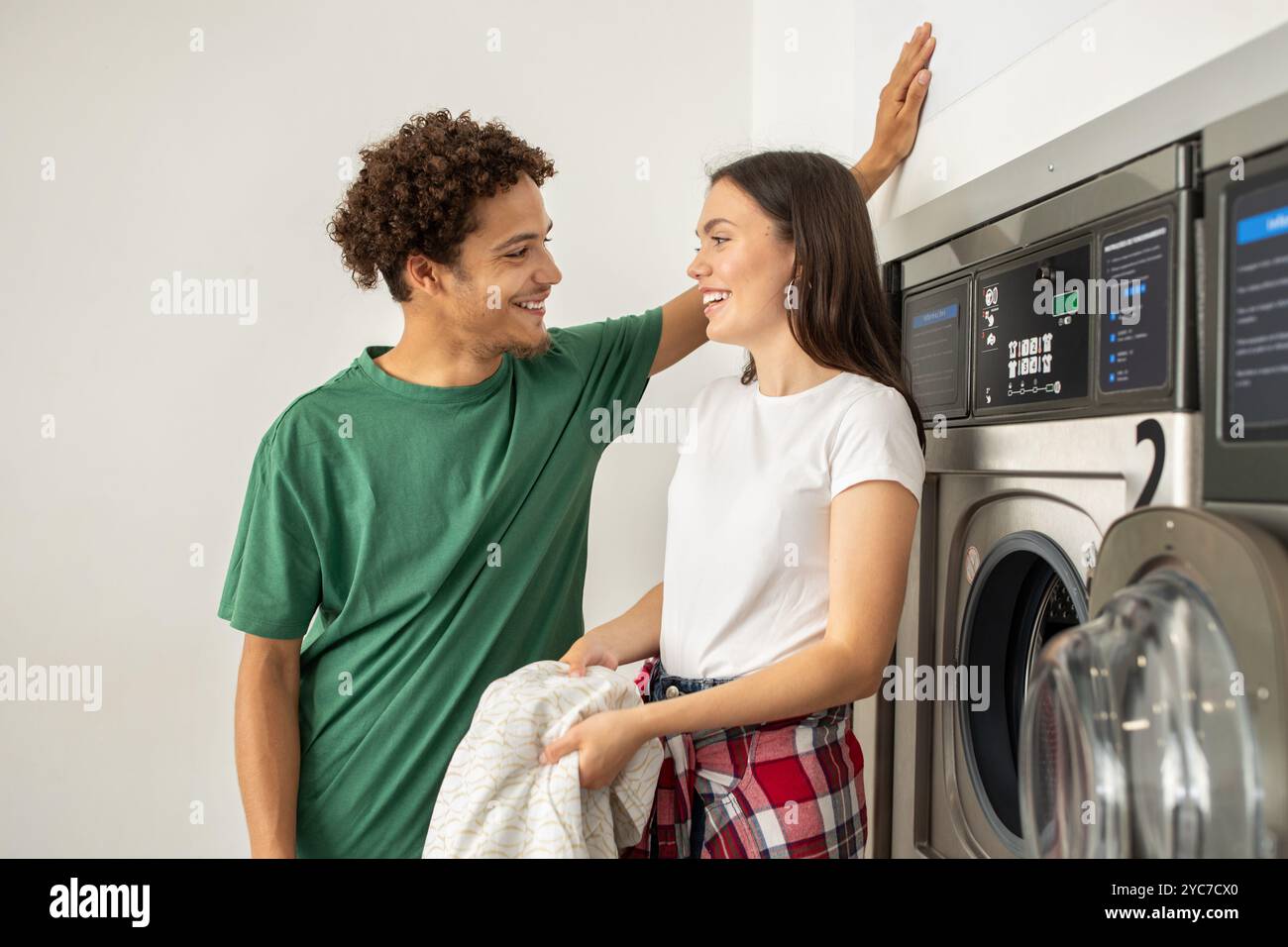 Jeune couple partageant un moment joyeux tout en faisant la lessive dans une laverie moderne Banque D'Images