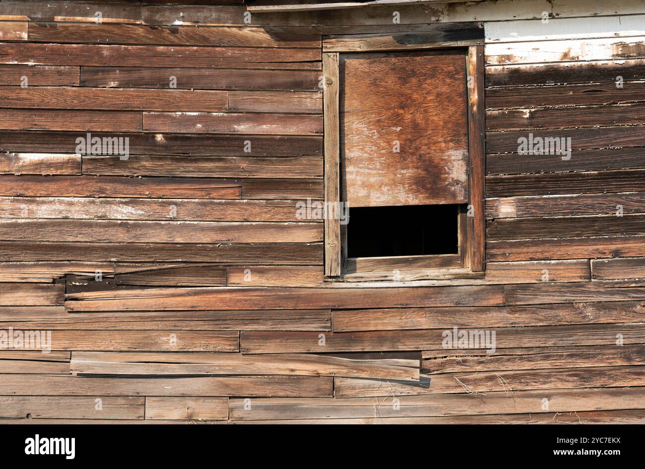 Vieux mur extérieur en bois d'un bâtiment avec fenêtre le vieux mur extérieur en bois du bâtiment arboré montre le parement altéré sans peinture visible. Banque D'Images