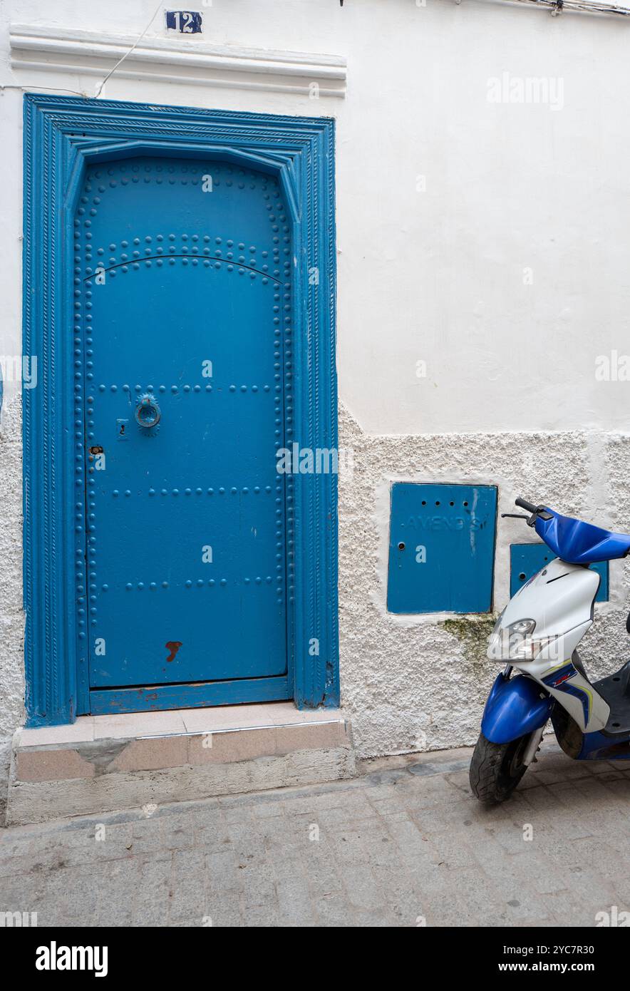 Porte cloutée bleue dans un mur blanc avec scooter bleu et blanc, zone de Kasbah, Tanger, Maroc Banque D'Images