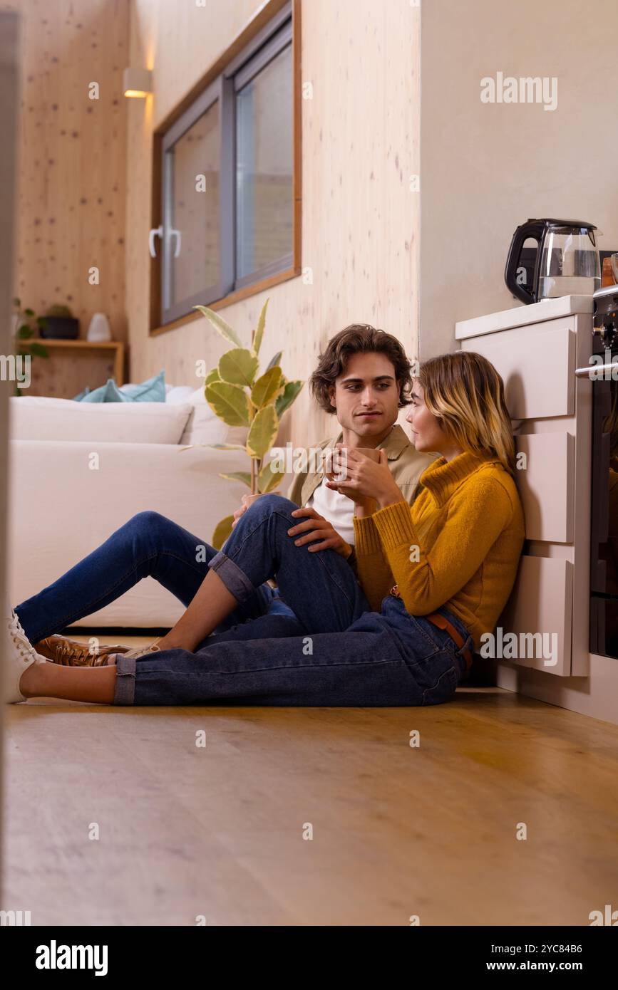 Couple assis sur le sol de la cuisine, partageant des boissons chaudes, profitant d'un moment à la maison confortable Banque D'Images