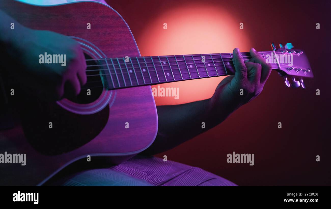 Concert de guitare. Performance musicale. Homme musicien artiste mains jouant des accords sur un instrument à cordes acoustique sur fond sombre avec une lumière néon brillante. Banque D'Images