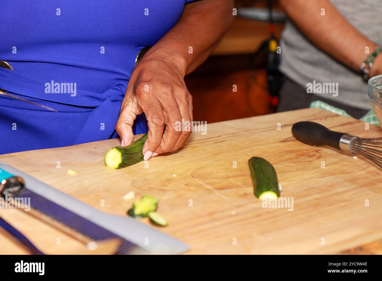 Une femme noire africaine dans une cuisine montrant ses mains couper un concombre sur une table de cuisine en bois Banque D'Images