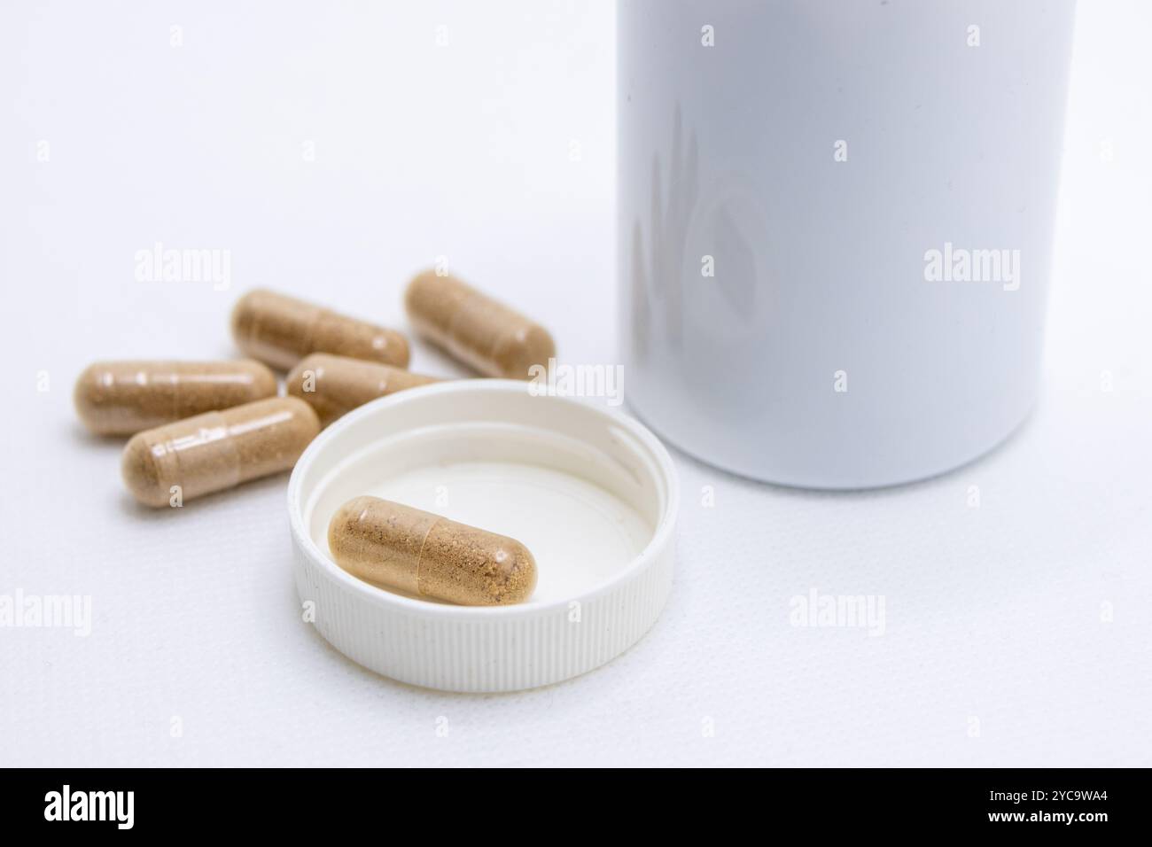 Les capsules de phytothérapie se déversent d'une bouteille blanche sur un fond blanc Banque D'Images