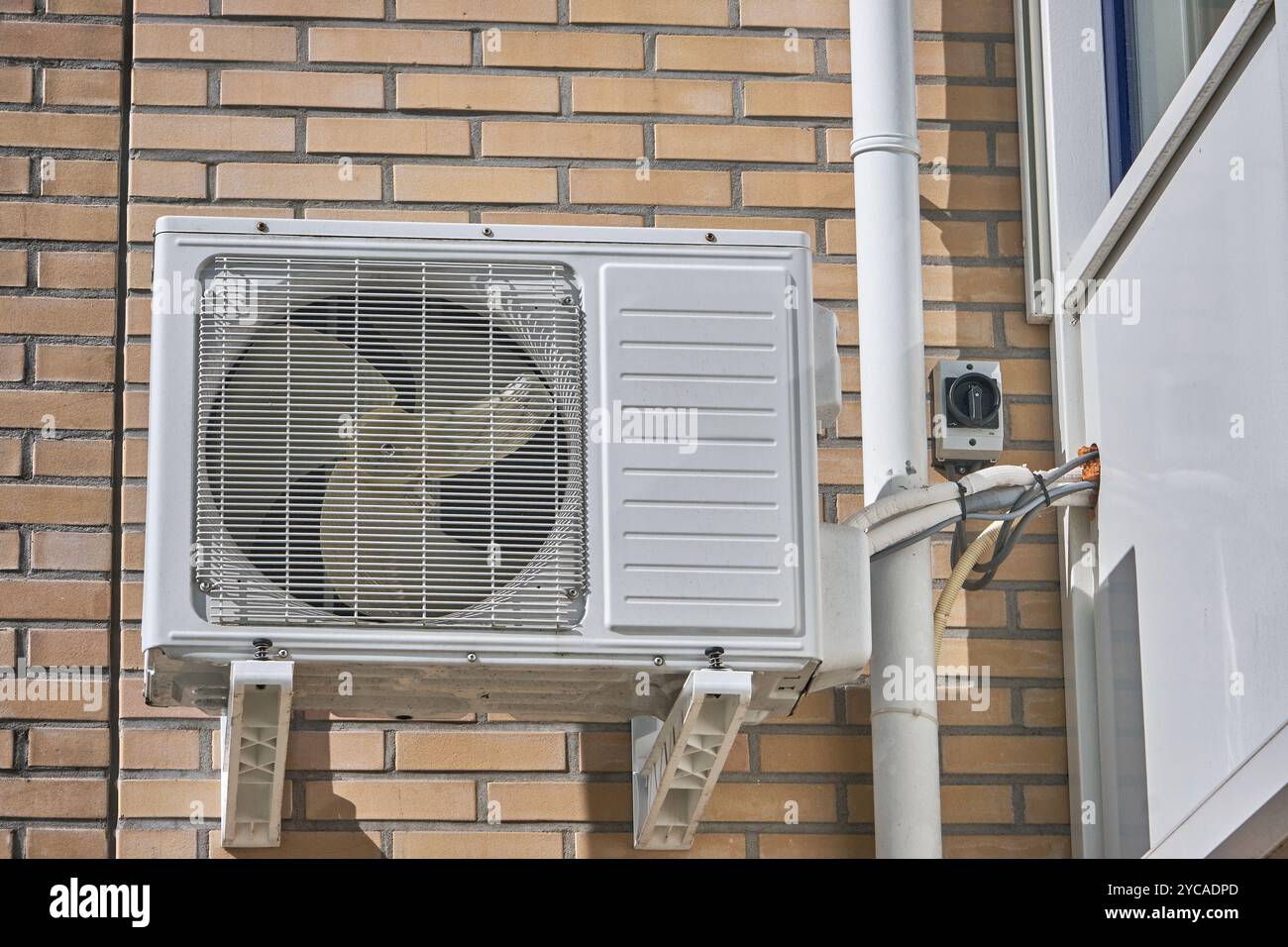Unité de pompe à chaleur moderne à source d'air montée à l'extérieur d'une résidence, contre un mur de briques légères, démontrant une technologie économe en énergie pour le chauffage. Banque D'Images