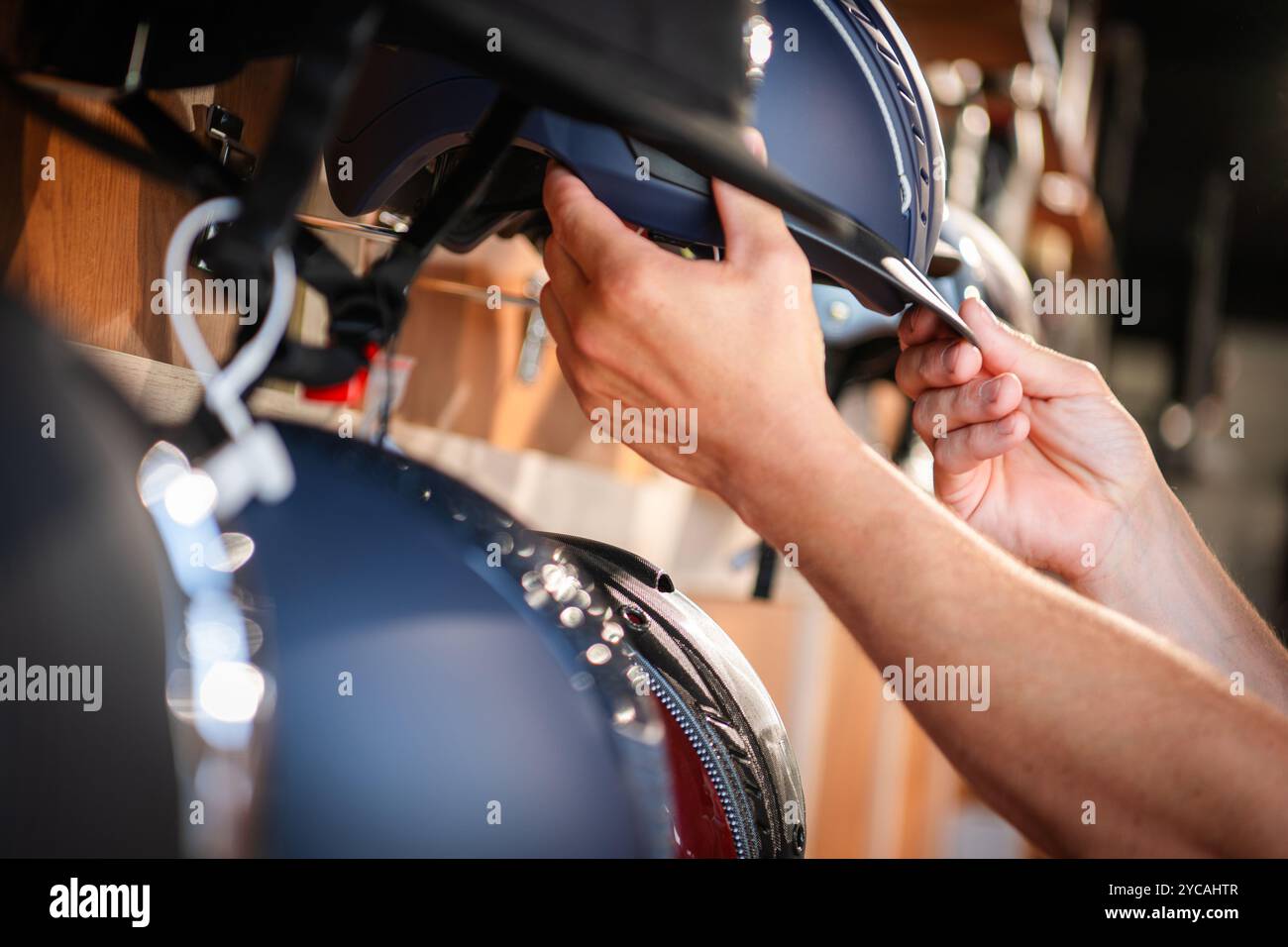 Une personne ajuste soigneusement un casque d'équitation bleu tout en parcourant la sélection dans un magasin. Le cadre est bien éclairé, mettant en vedette divers casques. Banque D'Images