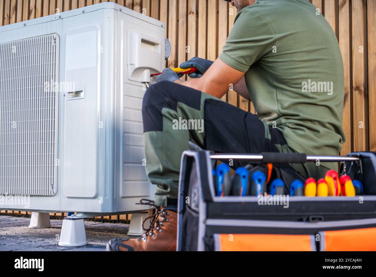 Un technicien travaille à l'entretien d'une unité de climatisation extérieure, en utilisant divers outils et équipements dans un environnement résidentiel. Banque D'Images