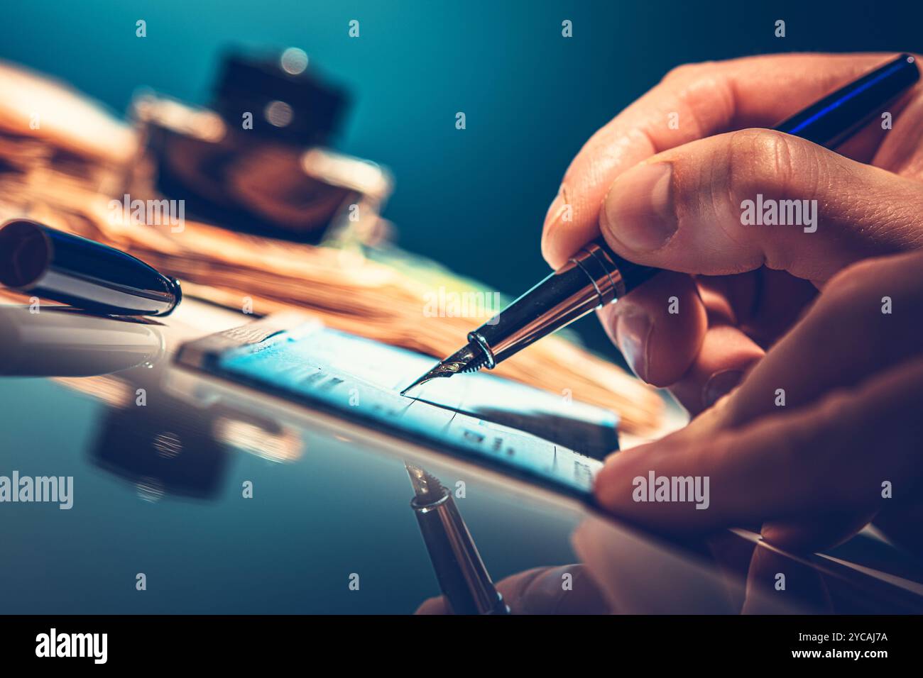 Une main tient un stylo plume, écrivant soigneusement un chèque de banque, avec un pot d'encre à proximité sur une surface réfléchissante, créant une atmosphère élégante dans l'espace de travail. Banque D'Images