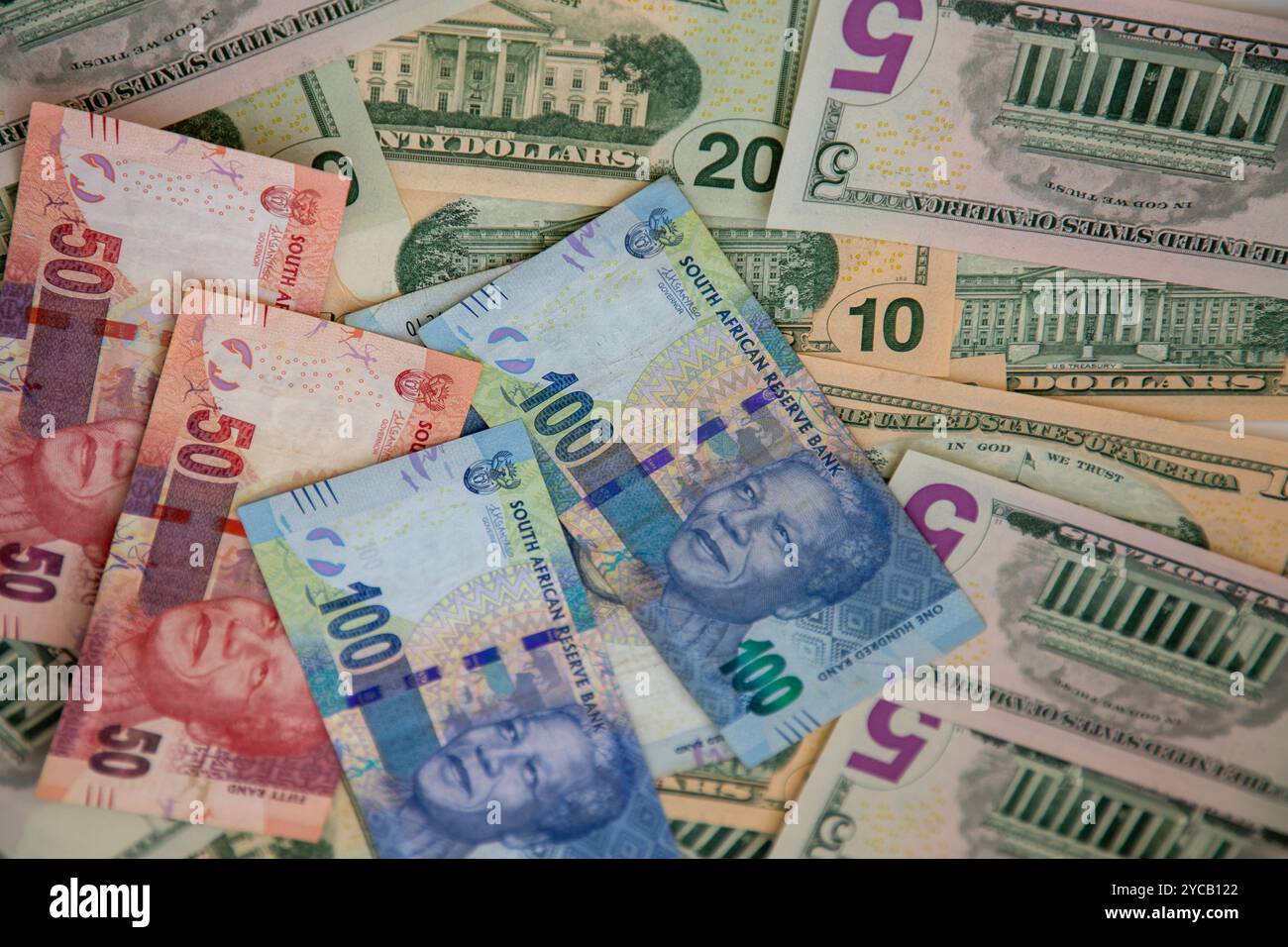 Focus sélectif sur les billets de monnaie sud-africains R50 et R100 avec différentes coupures de billets en dollars américains derrière eux. Banque D'Images