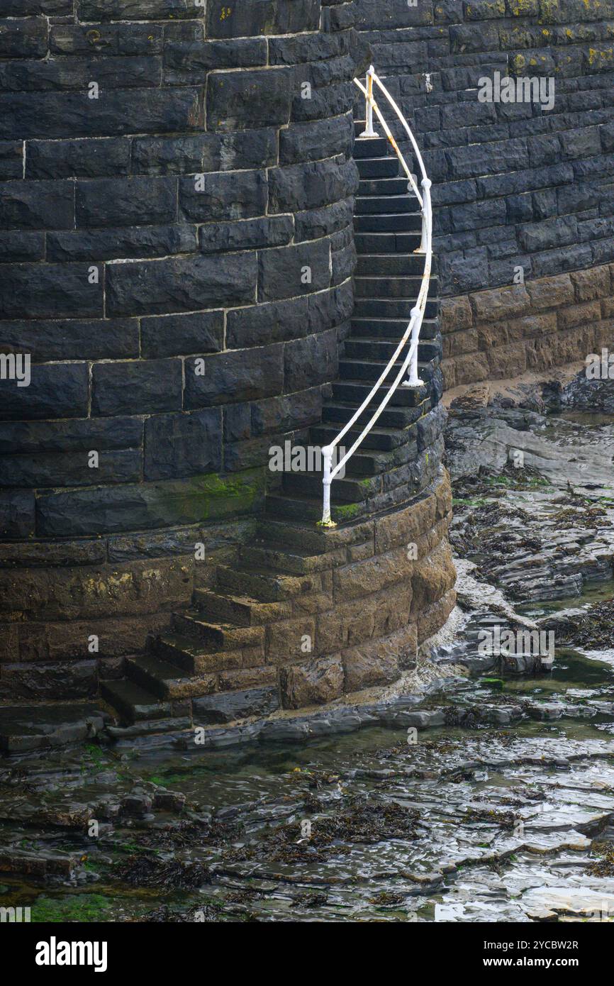 Balustrade en métal blanc courbé menant aux marches de la plage rocheuse avec la marée à Aberystwyth Banque D'Images