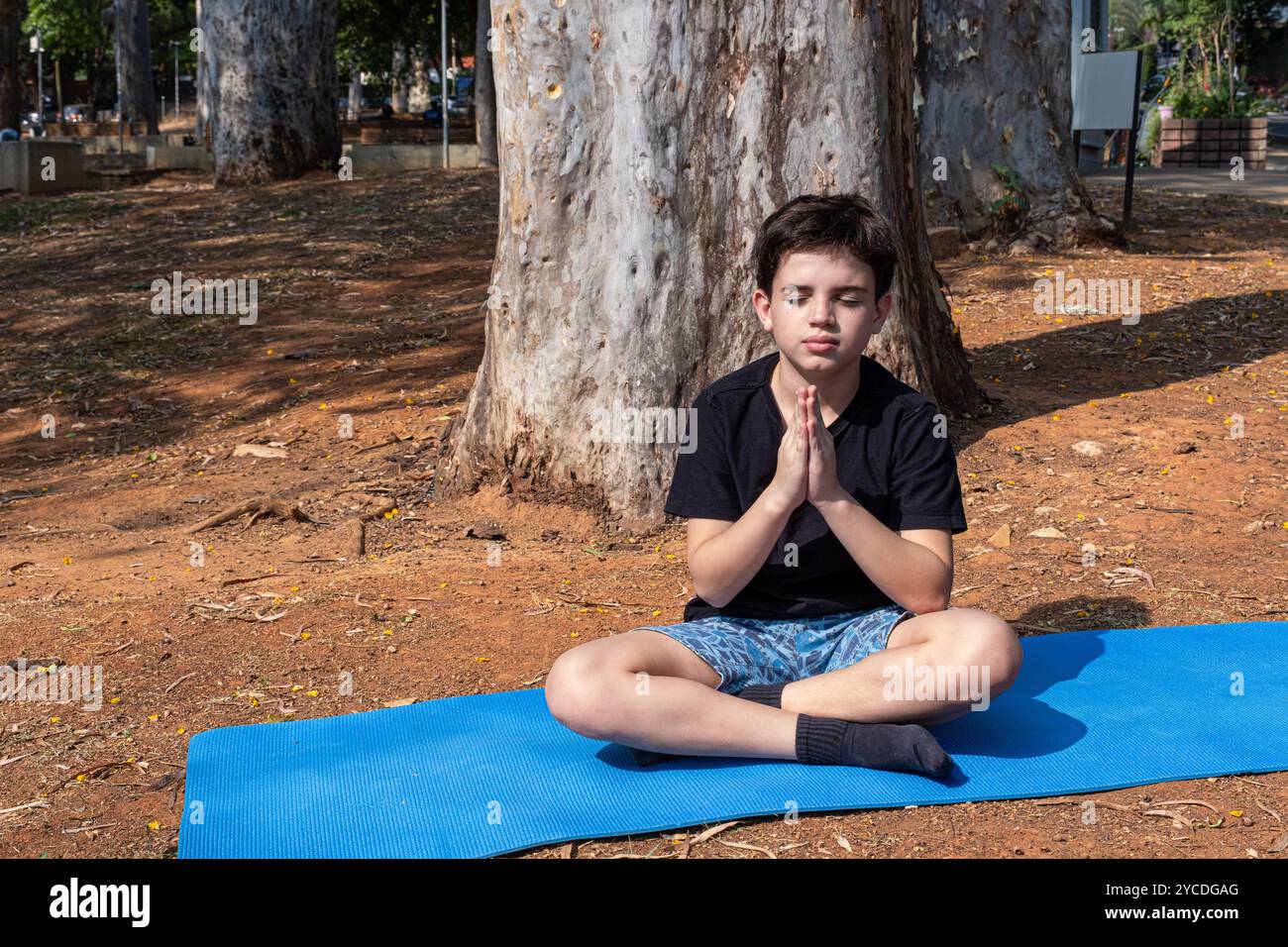 Enfant brésilien assis sur un tapis de yoga et pratiquant la respiration en classe extérieure 1. Banque D'Images