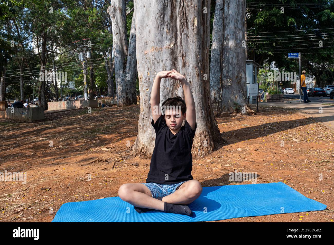Enfant brésilien assis sur un tapis de yoga et étirant en classe extérieure 6. Banque D'Images