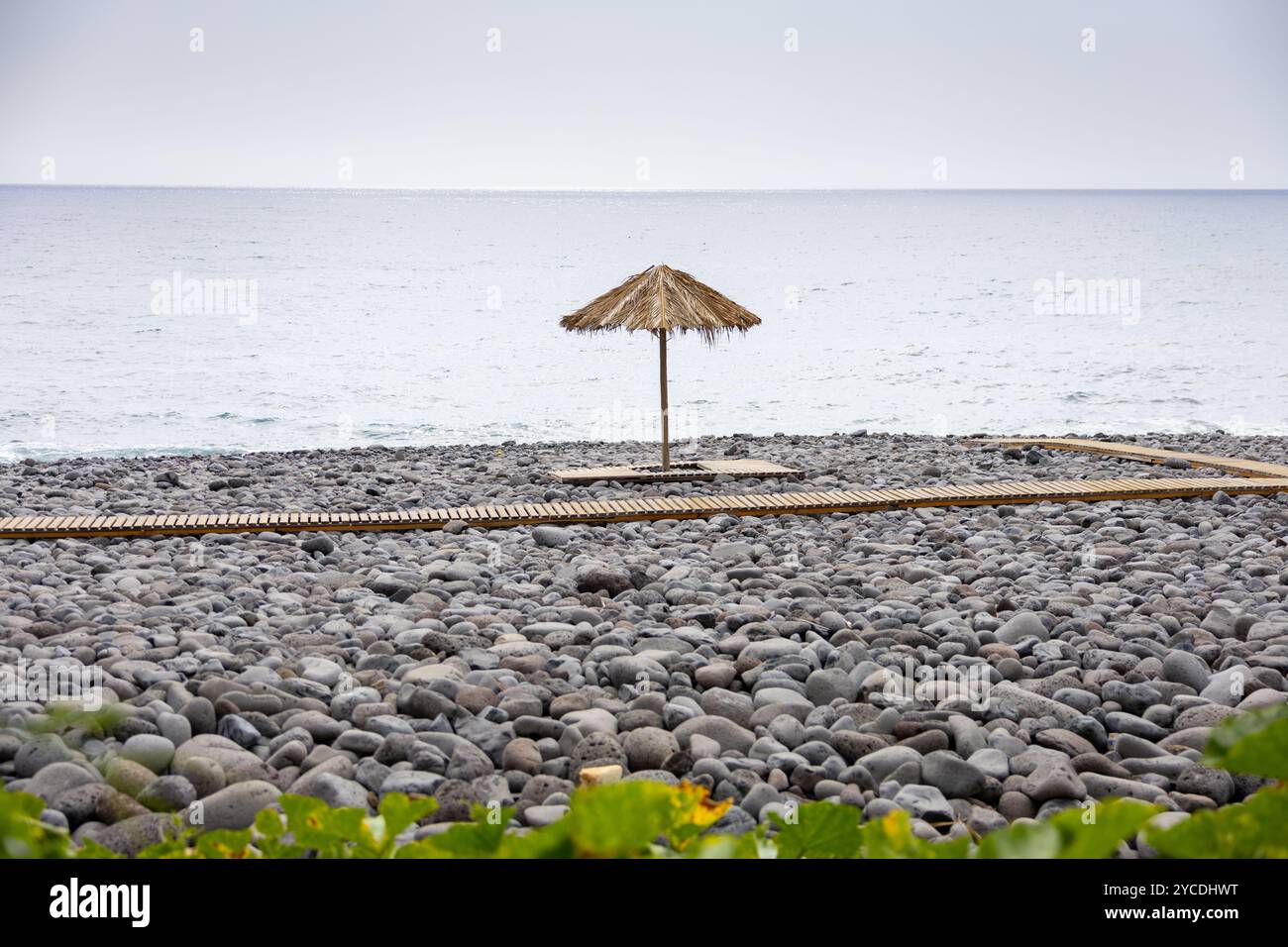 Plage de Praia dos Pescadores, composée de galets de basalte et de sable noir avec parasols en paille et terrasses en bois. Île de Madère, Portugal Banque D'Images