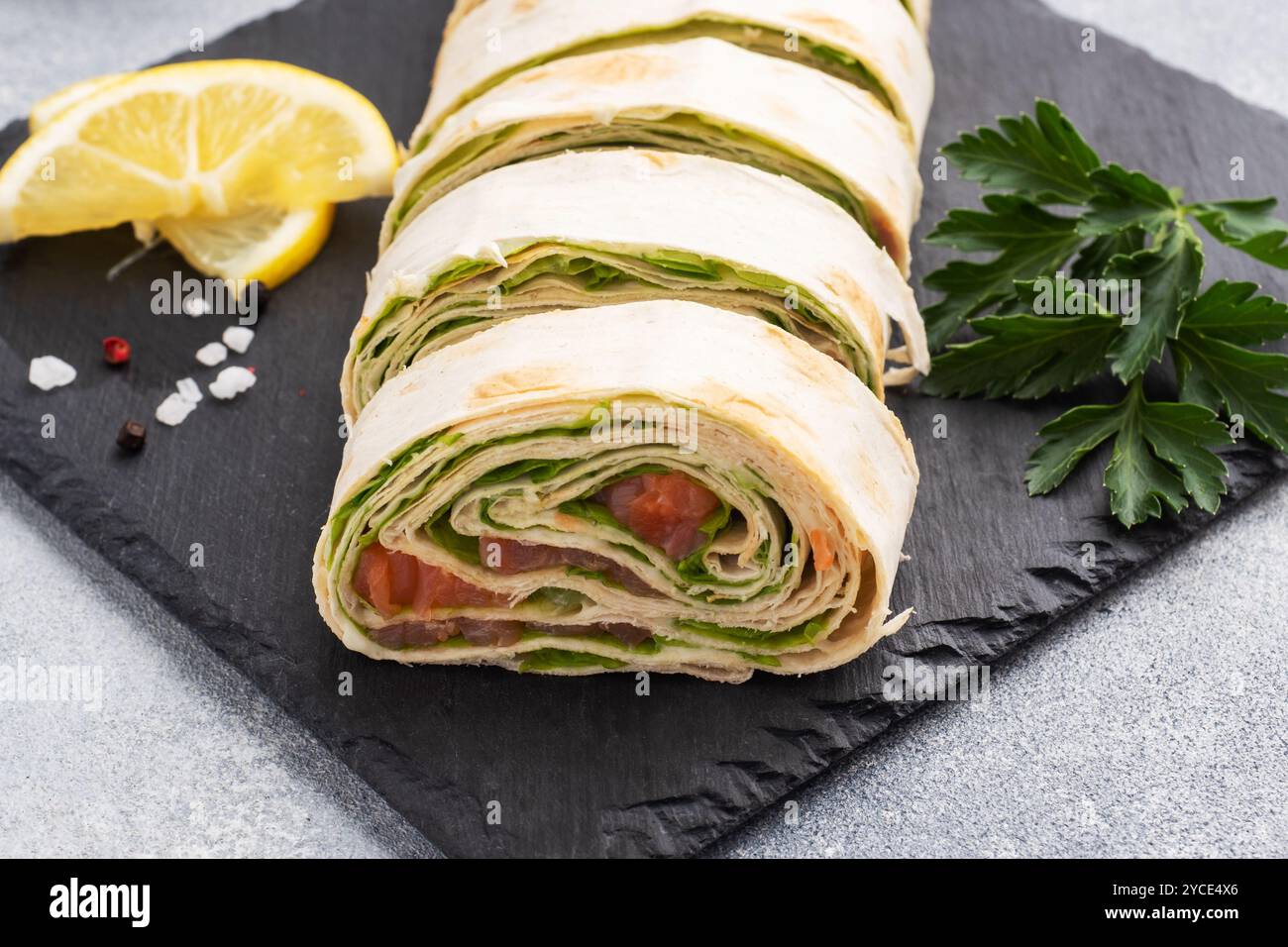 Rouleaux de pain pita fin et saumon rouge salé avec feuilles de laitue sur un support en ardoise, fond en béton gris. Copier l'espace Banque D'Images Rouleaux de pain pita fin et saumon rouge salé avec feuilles de laitue sur un support en ardoise, fond en béton gris. Copier l'espace Banque D'Images