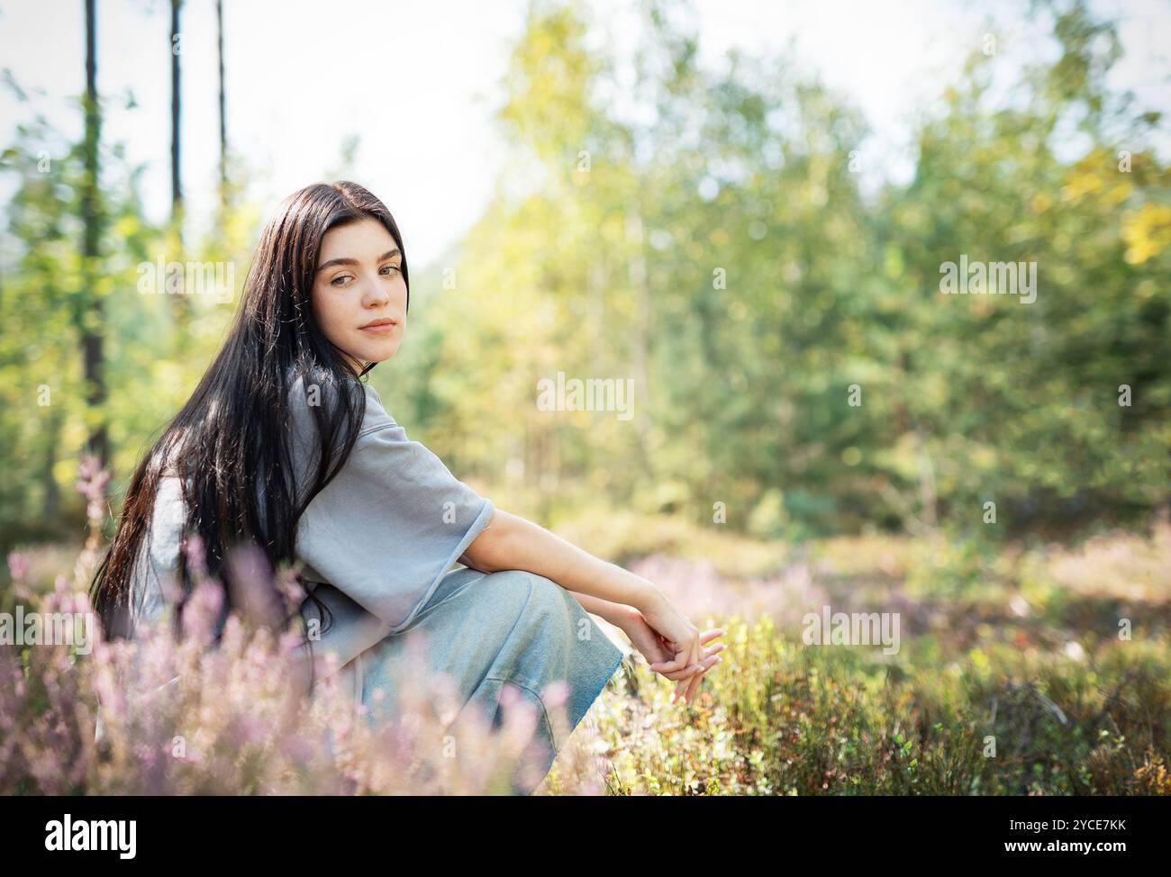 Une jeune femme est assise tranquillement sur le sol de la forêt, ses longs cheveux descendant en cascade dans son dos. Elle apparaît profondément dans la pensée, entourée de fleurs sauvages en fleurs Banque D'Images