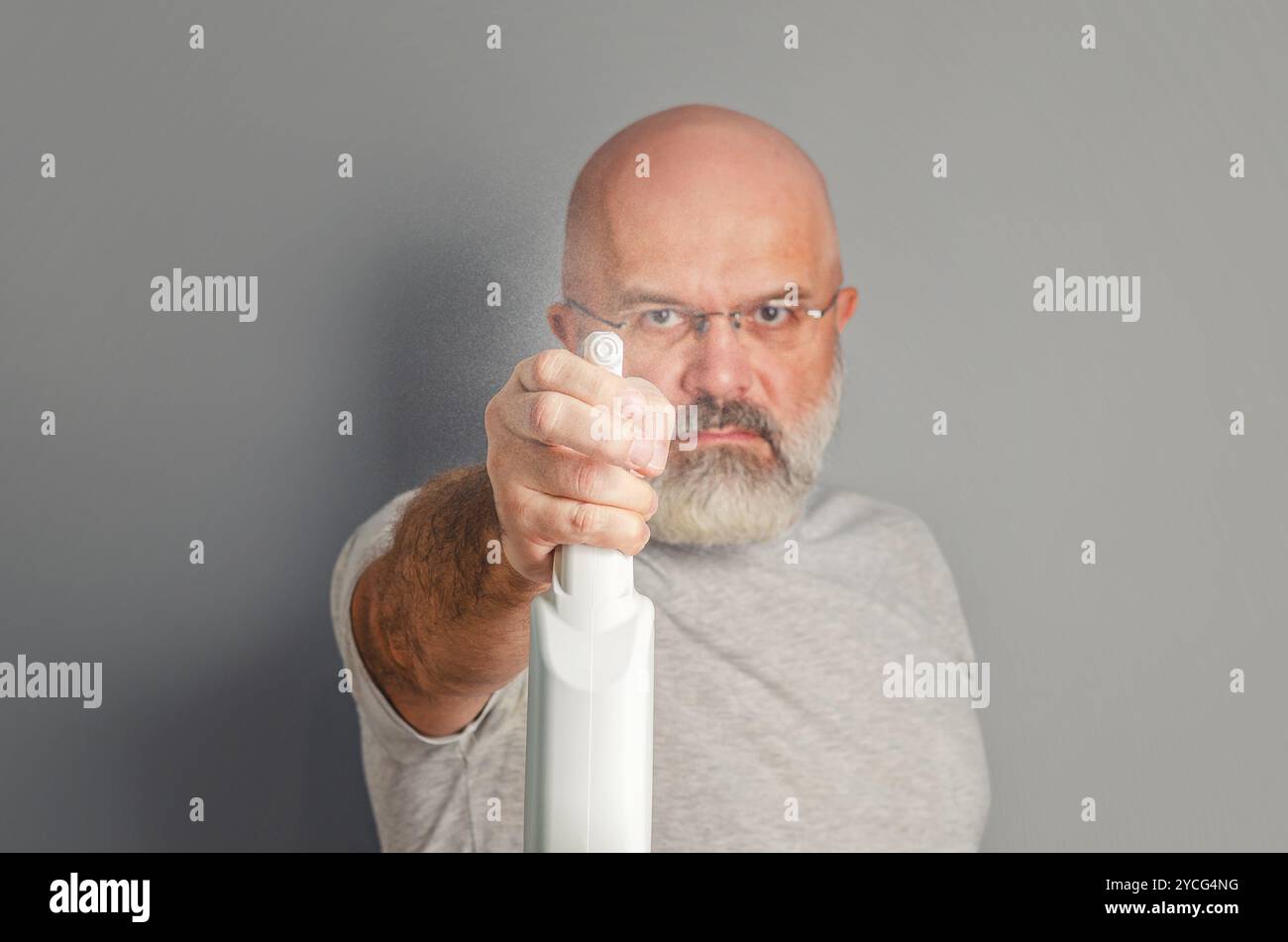 L'homme barbu dans des lunettes tient le flacon pulvérisateur comme s'il pointait le pistolet vers la caméra. Publicité humoristique Banque D'Images