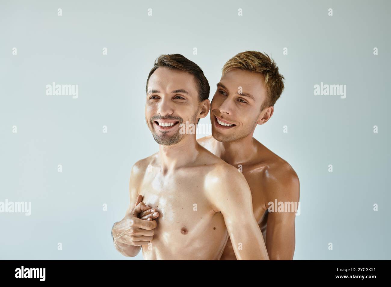 Deux hommes souriants partagent une étreinte chaleureuse, rayonnant de bonheur et d'amour dans un espace calme. Banque D'Images
