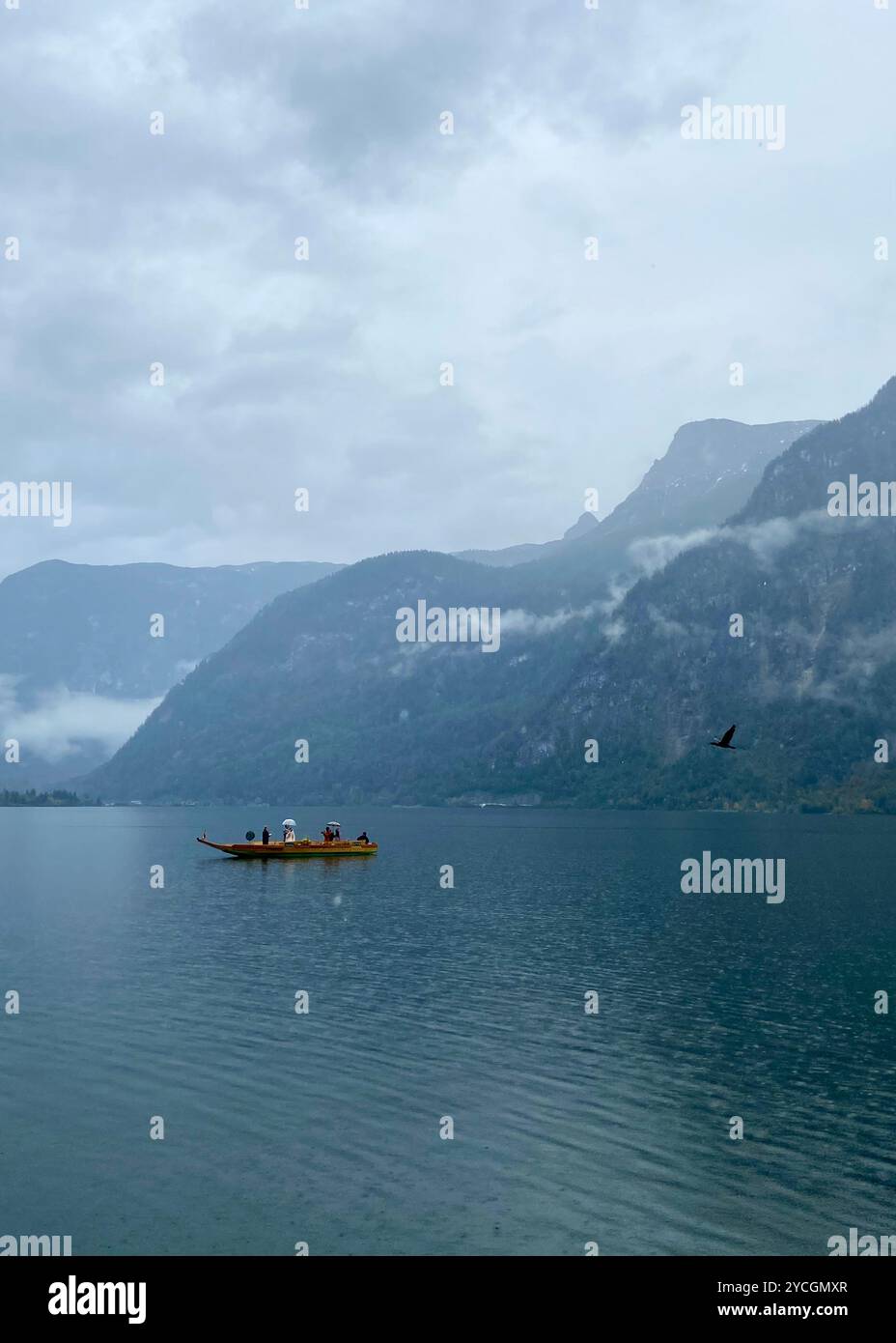 Hallstatt, Autriche - 2 octobre 2024 : couple se marie sur un bateau en bois sous la pluie sur le lac Hallstatt, entouré par les Alpes brumeuses un jour nuageux Banque D'Images