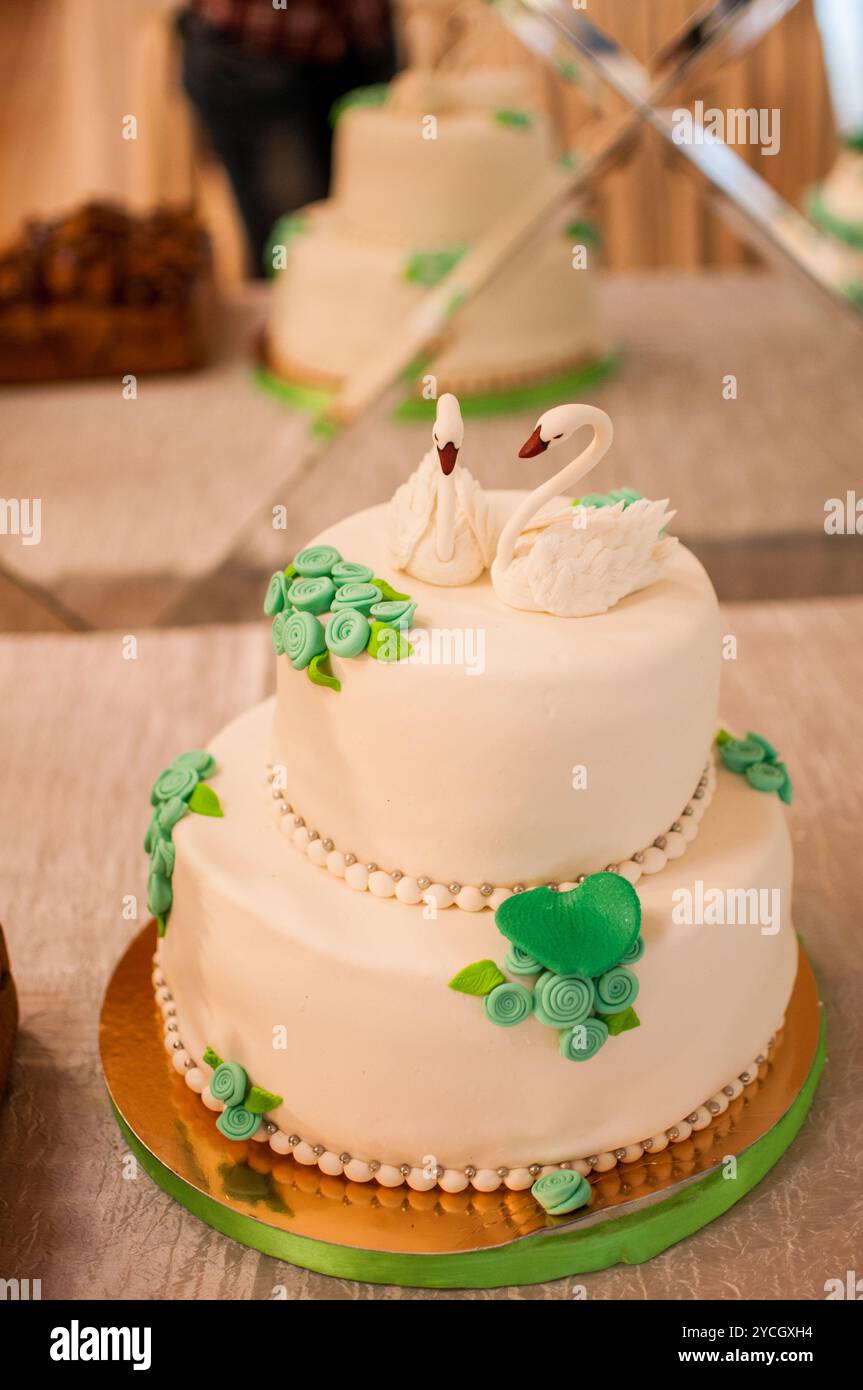 Elégant gâteau de mariage à deux niveaux avec des toppers de cygne et des accents floraux. Banque D'Images