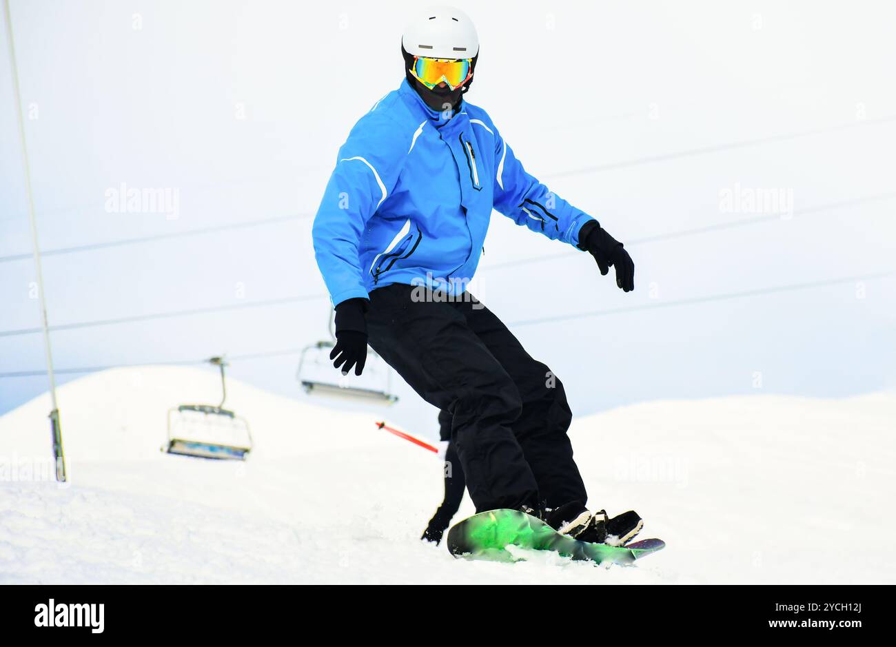 gros plan cavalier de snowboard décontracté dans une tenue noire bleue regarde vers le bas à la caméra isolée dans un fond neigeux blanc. Vacances d'hiver avec montagnes sportives Banque D'Images