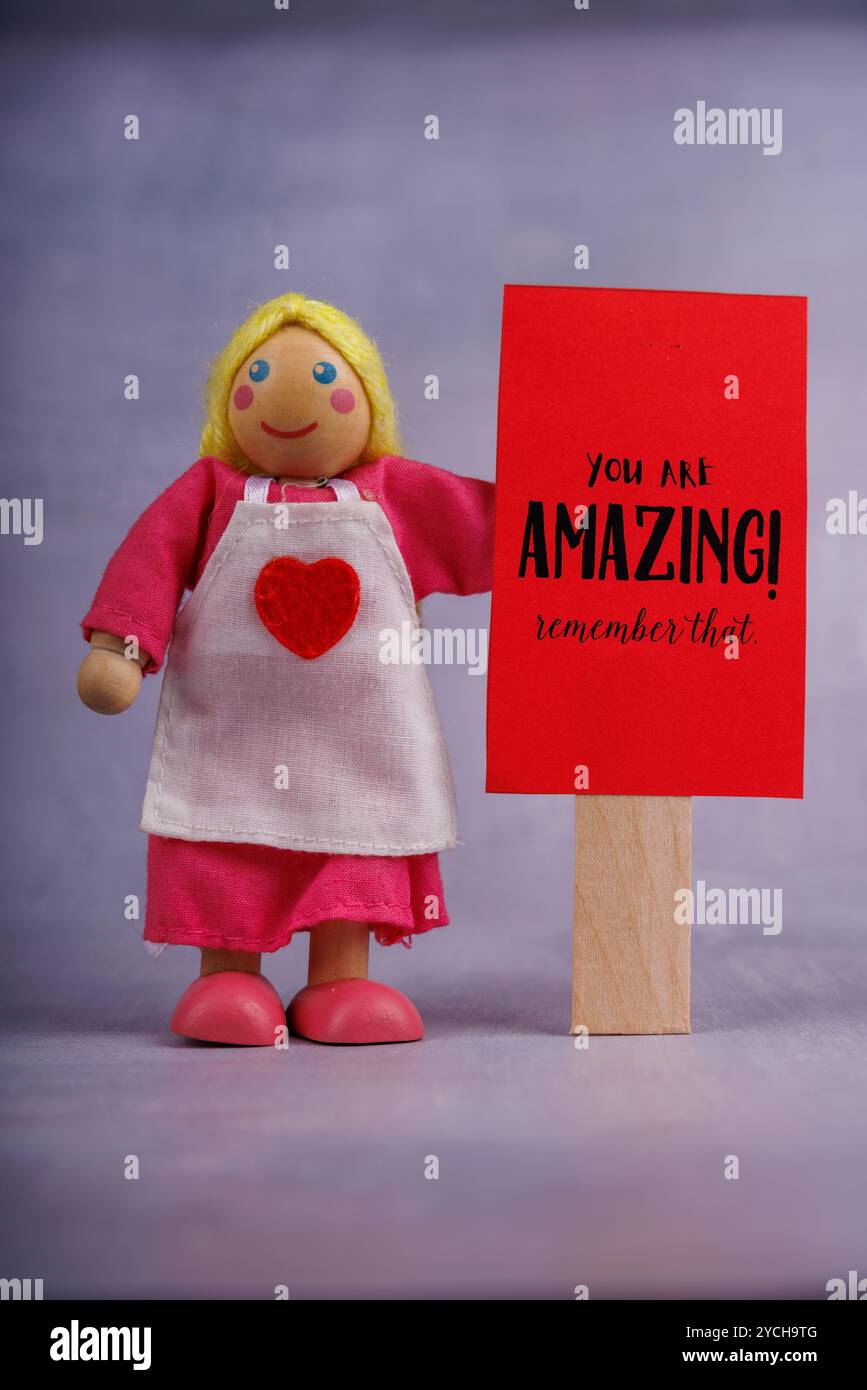 Une poupée en bois tient une bannière rouge affichant une phrase de motivation. La photo rayonne d'énergie positive et d'encouragement avec un messa simple et inspirant Banque D'Images