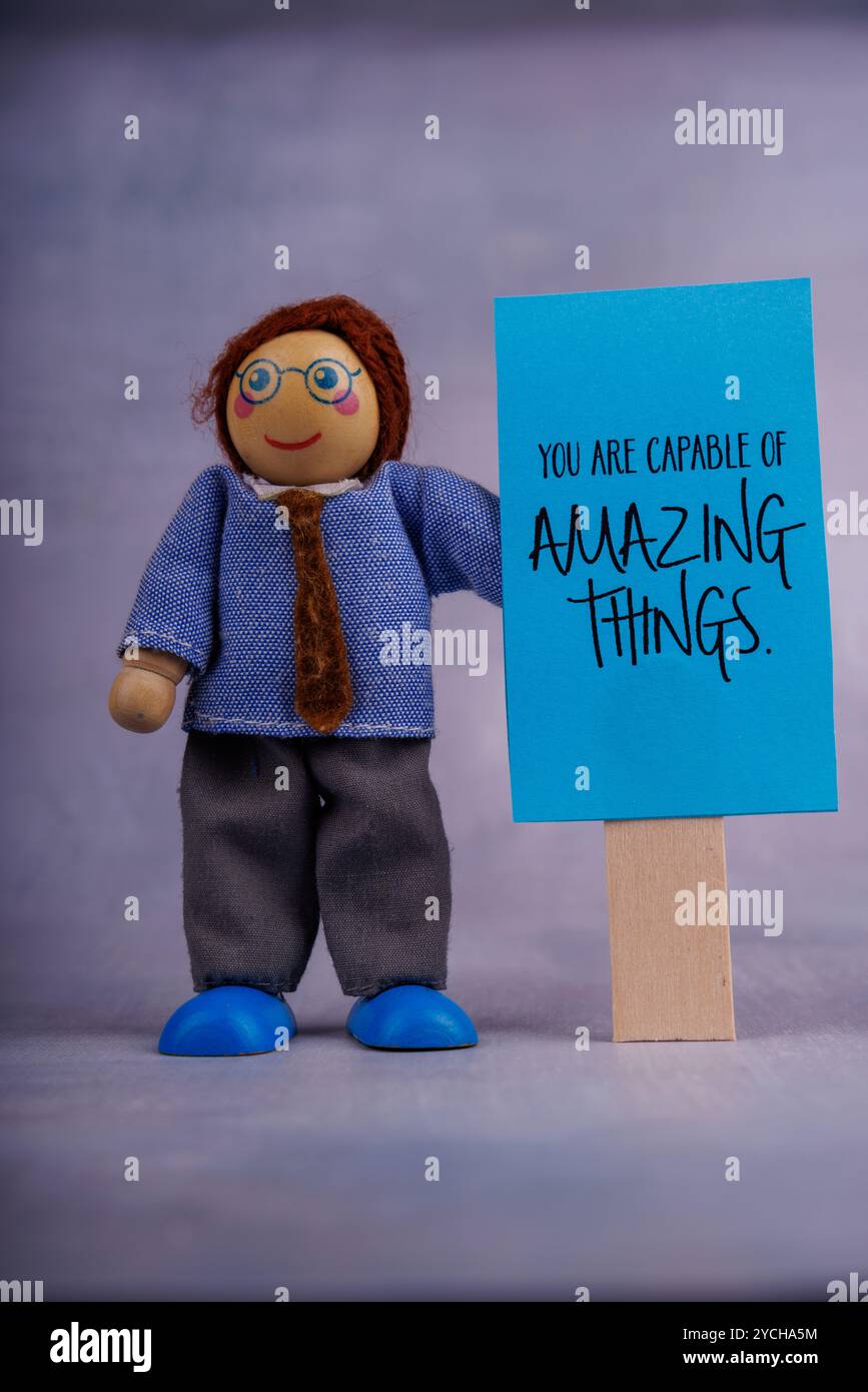 Une figurine de jouet en bois présente un signe bleu avec un message inspirant. La photo rayonne une énergie positive, offrant un léger coup de pouce de motivation Banque D'Images