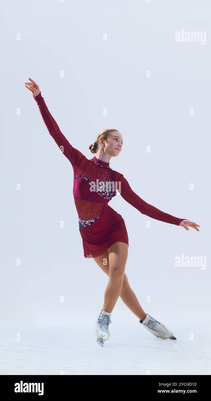 Jeune patineuse jouant dans une posture gracieuse, étendant ses bras vers l'extérieur, glissant doucement sur la glace, isolée sur fond blanc. Banque D'Images