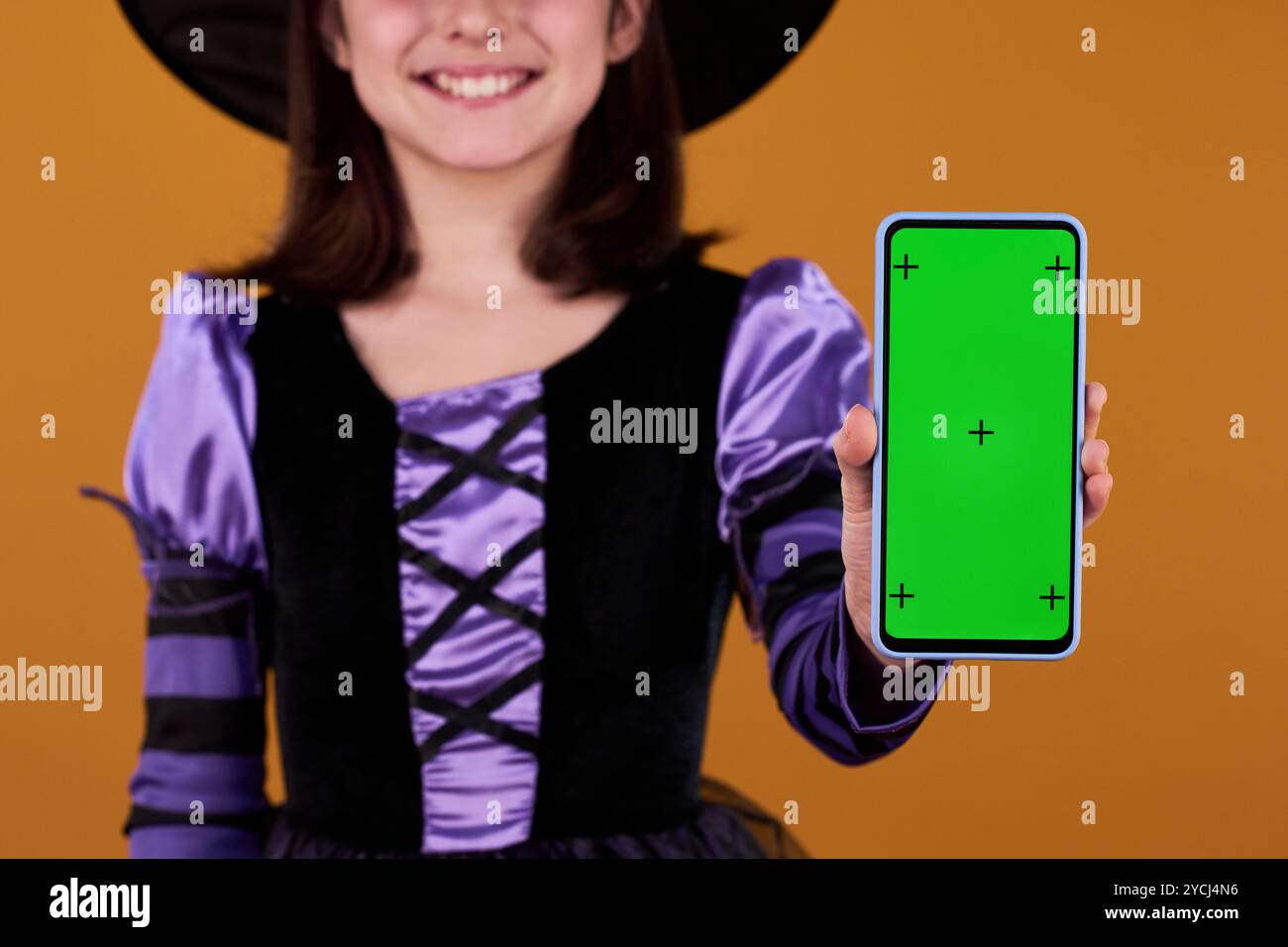 Concentrez-vous sur l'écran chromakey du smartphone tenu par une jeune fille souriante portant le costume de sorcière d'Halloween Banque D'Images