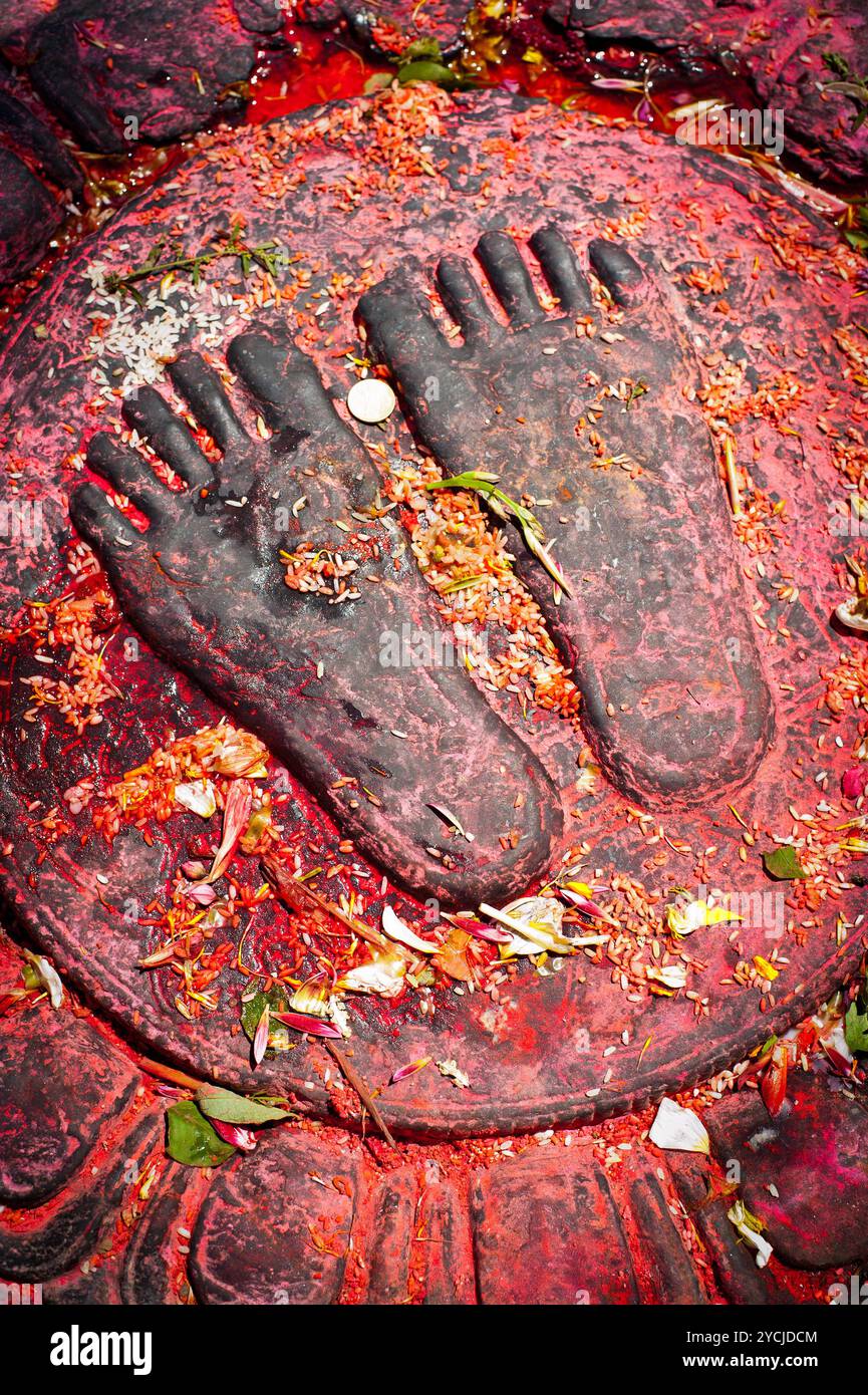 Bouddha peint en rouge deux pieds avec des fleurs de riz et des offrandes de pièces près du sanctuaire bouddhiste Swayambhunath Stupa. Temple des singes. Népal Banque D'Images