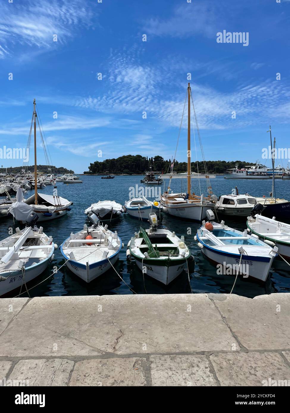 voiliers amarrés dans une marina européenne. Le ciel est bleu vif avec quelques nuages et une île peut être vue au loin. - Image de stock capturée avec un smartphone