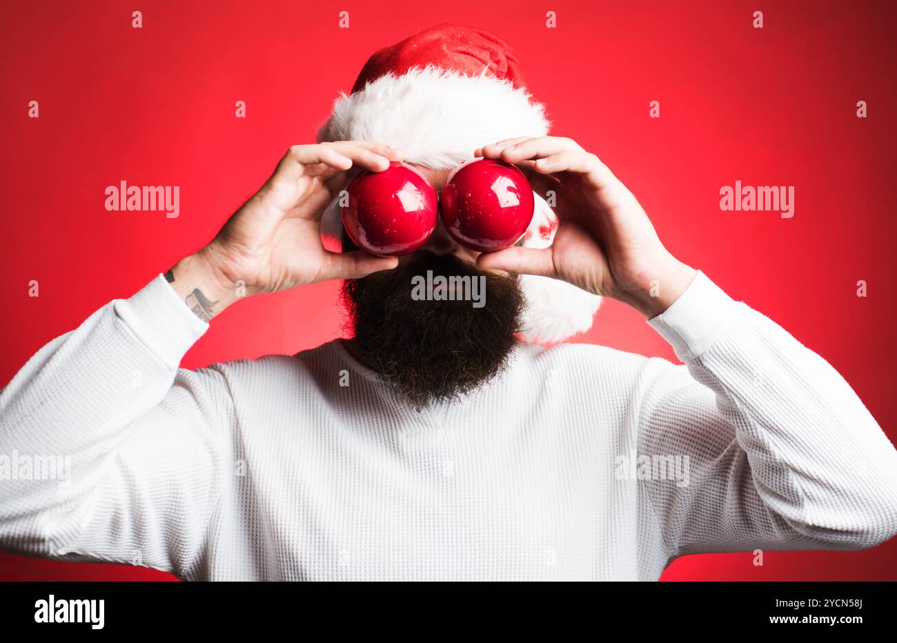 Père Noël avec des boules de Noël. Homme barbu dans le chapeau de Père Noël couvrant les yeux avec des balles de jouet du nouvel an. Boules de Noël décoratives pour arbre de Noël Banque D'Images