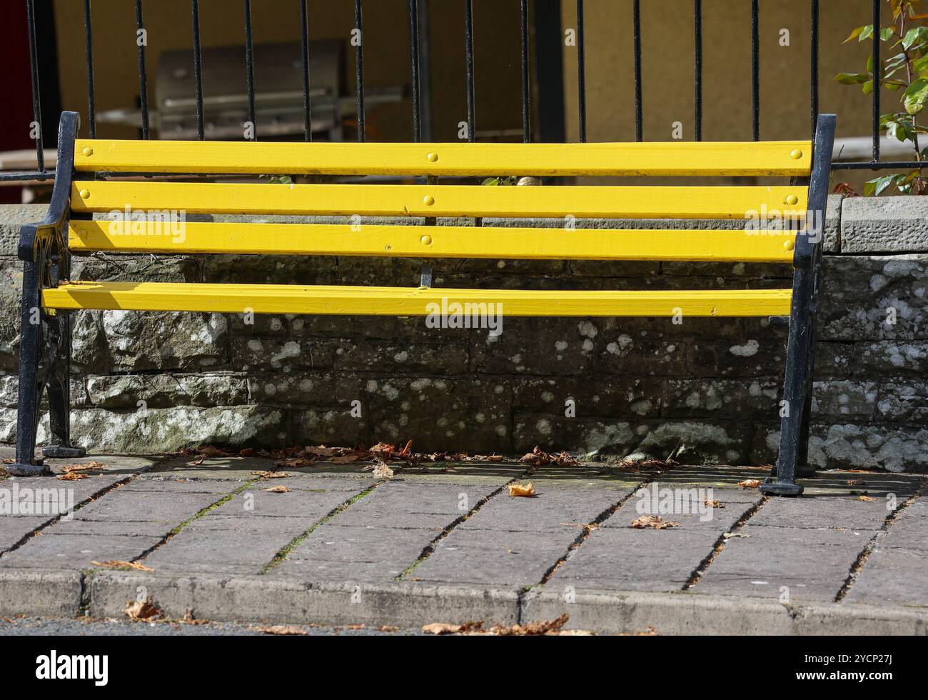 Sièges publics banquette en bois jaune bras en métal noir sur le trottoir public village irlandais rural Irlande Glaslough. Banque D'Images